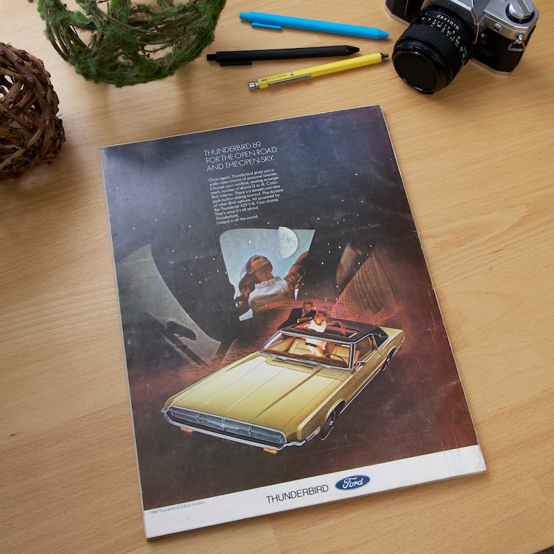 May include: A vintage advertisement for the 1969 Ford Thunderbird. The ad features a yellow Thunderbird driving on a dark road under a starry sky. The text reads "Thunderbird '69 for the open road and the open sky".