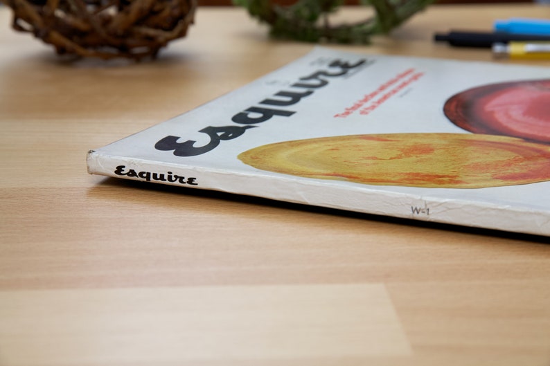 May include: A white magazine with the word "Esquire" printed in black on the cover. The magazine is lying on a wooden surface.