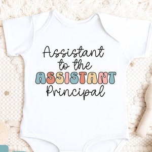 May include: White baby onesie with the text "Assistant to the Assistant Principal" in colorful, retro-style letters.