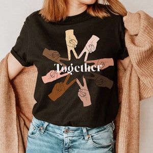 May include: Black t-shirt with a graphic of hands in a circle forming a star shape. The hands are different skin tones and the text "Together" is in the center of the star.