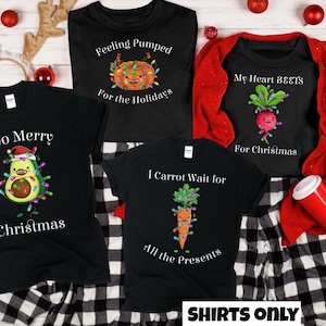 May include: Four black t-shirts with Christmas-themed vegetable designs. The shirts feature an avocado, a pumpkin, a carrot, and a beet, each with Christmas lights. The text on the shirts reads "Avo Merry Christmas", "Feeling Pumped for the Holidays", "I Carrot Wait for All the Presents", and "My Heart BEETS for Christmas".