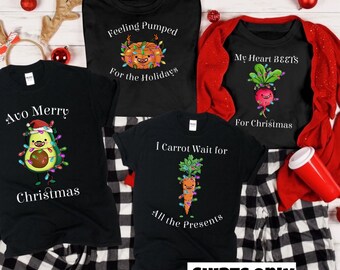 May include: Four black t-shirts with Christmas-themed vegetable designs. The shirts feature an avocado, a pumpkin, a carrot, and a beet, each with Christmas lights. The text on the shirts reads "Avo Merry Christmas", "Feeling Pumped for the Holidays", "I Carrot Wait for All the Presents", and "My Heart BEETS for Christmas".
