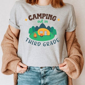 May include: Gray t-shirt with the text "Camping out in third grade" and a cartoon image of a camper in a forest setting.