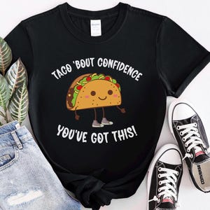 May include: Black t-shirt with a white graphic of a cartoon taco with the text "Taco 'Bout Confidence You've Got This!"