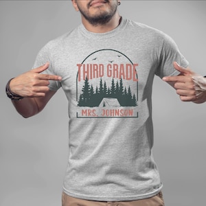 May include: Grey t-shirt with a graphic of a tent in a forest with the text "Third Grade" and "Mrs. Johnson" printed on it.