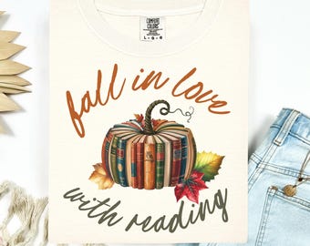 May include: Cream-colored sweatshirt with a pumpkin made of books and the text "Fall in love with reading" in brown and green. The pumpkin has a green stem and is surrounded by fall leaves.