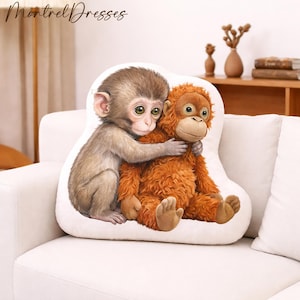 May include: A decorative pillow featuring two adorable monkeys hugging. One monkey is brown with a light brown face and the other is orange with a light brown face. The pillow is white and has the text "Montrel Dresses" in the upper left corner.
