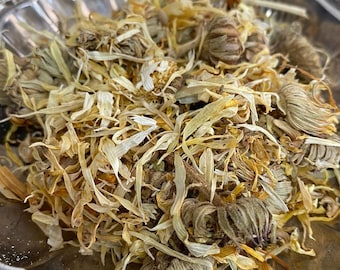 May include: A silver bowl filled with dried yellow and white flower petals and buds. The petals are loose and scattered throughout the bowl.