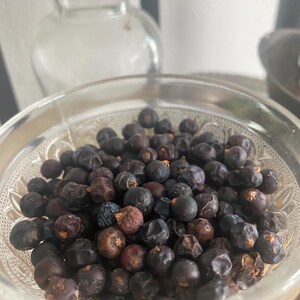 May include: A clear glass bowl filled with dark blue juniper berries.