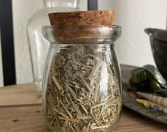 May include: A glass jar with a cork lid filled with dried herbs. The jar is sitting on a wooden surface.