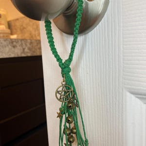 May include: A green tassel with a pentagram charm and bells hanging from a door knob.