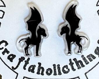 May include: A pair of black and white earrings featuring a silhouette of a winged horse, or a hippogriff, with a transparent background. The earrings are on a white background with the text "Craftaholicthings" written in black.