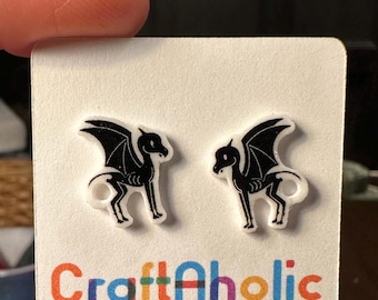 May include: A pair of black and white dragon-shaped earrings on a white card. The earrings have a skeletal design with wings. The card has the text "CraftAholic Things" in colorful letters.