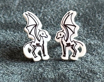 May include: A pair of white stud earrings with a black line drawing of a winged horse skeleton.