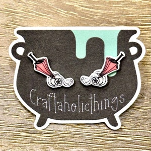 May include: A pair of pink and white earrings featuring a small umbrella and a cloud with a star. The earrings are displayed on a black cauldron with the text "Craftaholicthings".