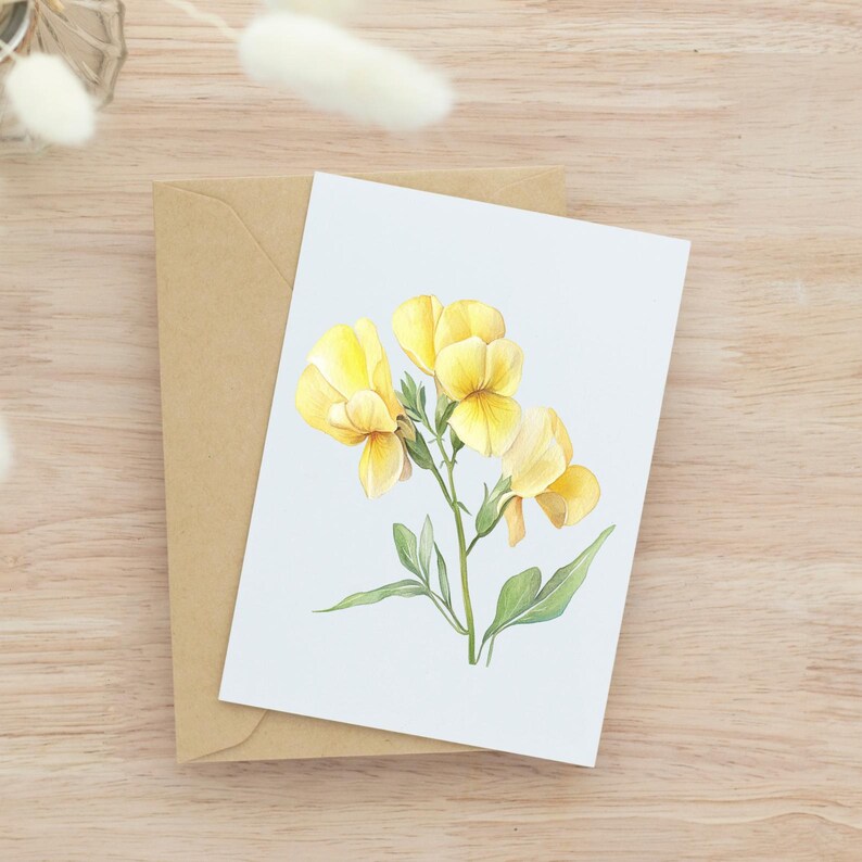 May include: A greeting card featuring a watercolor illustration of yellow flowers with green leaves. The card is on top of a brown envelope, set against a light wood grain background. The flowers have a delicate, detailed appearance.