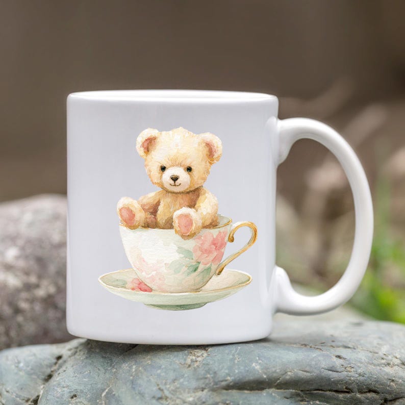 Puede incluir: Taza de cer&aacute;mica blanca con una ilustraci&oacute;n de acuarela de un oso de peluche sentado en una taza de t&eacute;. La taza y el platillo tienen un dise&ntilde;o floral con acentos rosas y verdes. La taza tiene un asa curva.