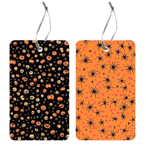 Pode incluir: Duas etiquetas de presente com tema de Halloween. Uma etiqueta apresenta um fundo preto com ab&oacute;boras laranja e um cord&atilde;o branco. A outra etiqueta apresenta um fundo laranja com teias de aranha pretas e um cord&atilde;o branco.