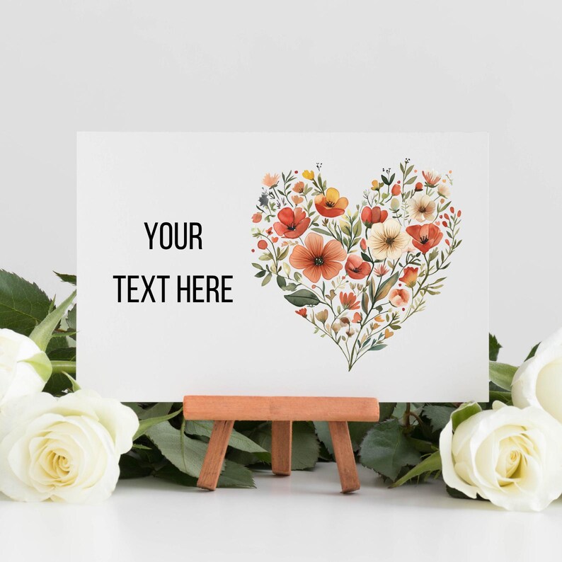 May include: A white card on a small wooden easel, featuring a heart-shaped floral design in shades of red, orange, and yellow. The card has the text "YOUR TEXT HERE" in black. White roses are in the foreground.