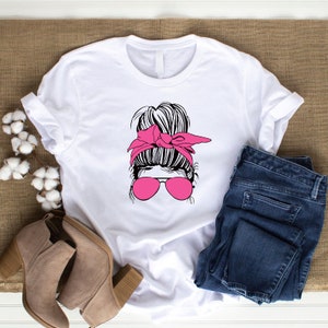 May include: White t-shirt with a graphic of a woman with a messy bun, pink sunglasses, and a pink headband.