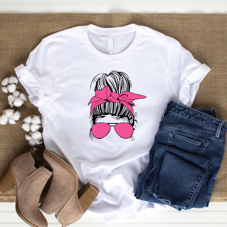 May include: White t-shirt with a graphic of a woman with a messy bun, pink sunglasses, and a pink headband.