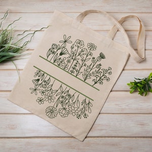 May include: A white canvas tote bag with a green line design of various flowers and leaves. The bag has two handles.
