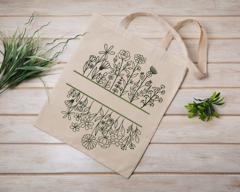 May include: A white canvas tote bag with a green line design of various flowers and leaves. The bag has two handles.