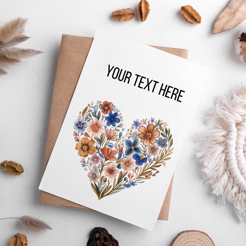 May include: A white greeting card with the text "YOUR TEXT HERE" in black. The card features a heart-shaped floral design in shades of blue, orange, and pink. The card is on a brown envelope.