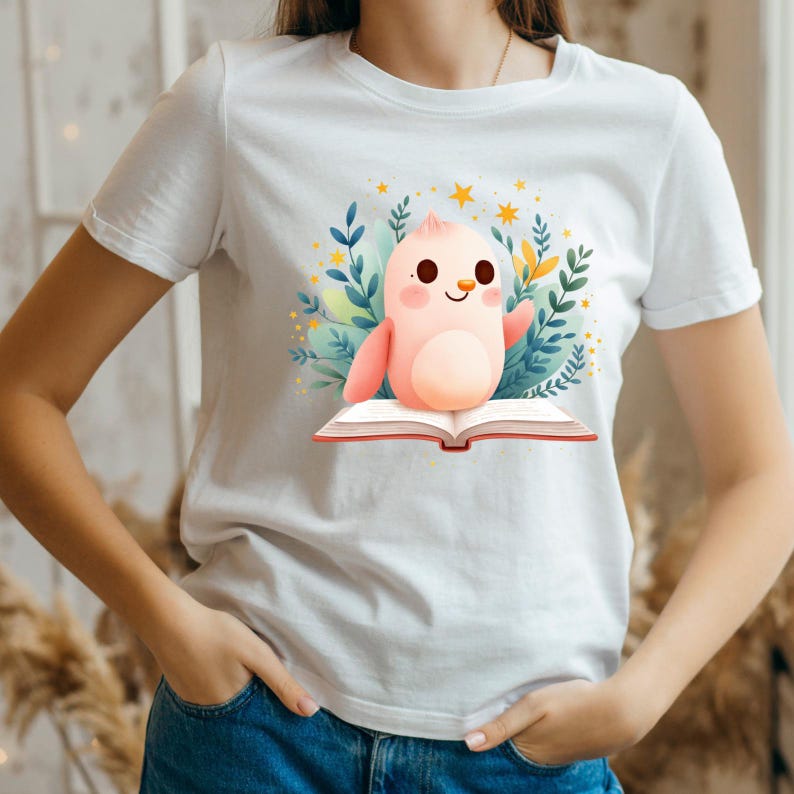 K&ouml;nnte beinhalten: Wei&szlig;es T-Shirt mit einer Cartoon-Illustration eines rosa Vogels, der auf einem offenen Buch sitzt. Der Vogel ist von Bl&auml;ttern, Sternen und Blumen umgeben. Das Design ist farbenfroh und skurril, perfekt f&uuml;r B&uuml;cherliebhaber und Fans niedlicher Illustrationen.