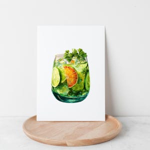 May include: A watercolour painting of a cocktail in a clear glass. The drink contains ice, lime and orange slices, and fresh herbs. The glass is set against a white background, and the painting is on a white rectangular surface.