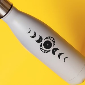 May include: A gray stainless steel water bottle with a black moon phase design. The bottle has a screw-on lid.