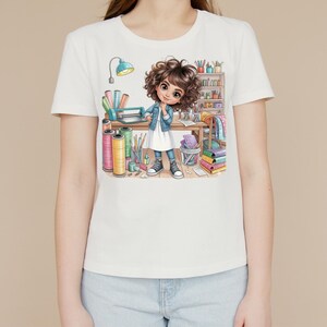 May include: A white short-sleeved t-shirt featuring a graphic illustration of a person with curly brown hair standing in a craft room. The character wears a denim jacket over a white dress and trainers, surrounded by spools of thread and supplies.