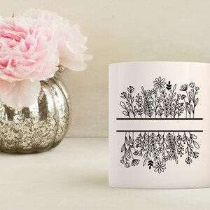 May include: White ceramic mug with a black line design of flowers and leaves. The flowers are upside down on the bottom half of the mug.
