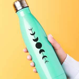 May include: A turquoise reusable water bottle with a black and white moon phase design. The bottle has a silver lid.
