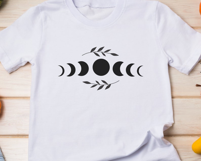 May include: White t-shirt with a black moon phases design. The design features a full moon, crescent moons, and a leafy branch.
