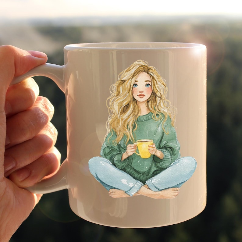 May include: A beige ceramic mug featuring a watercolor illustration of a woman with long blonde hair, blue eyes, and a green sweater. She is holding a yellow mug and wearing blue jeans. The mug is held by a hand.
