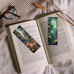 May include: Two colorful bookmarks with a fantasy forest scene. The bookmarks are made of paper and have a glossy finish. The forest scene features glowing trees, flowers, and a path leading through the woods.