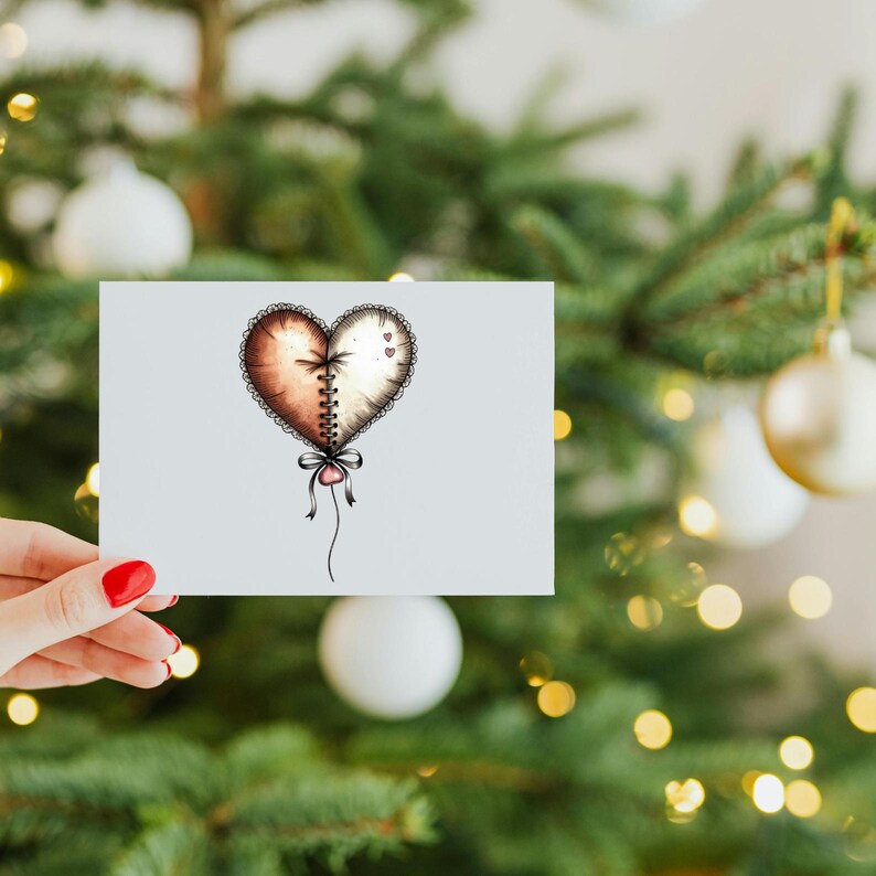 May include: A greeting card with a heart design, divided into brown and white halves, joined by a stitched seam. It has a decorative bow and string. The card is held in front of a Christmas tree with baubles.