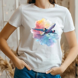 May include: White t-shirt featuring a colorful graphic of an airplane soaring through a vibrant cloud of pink, yellow, and blue hues. The airplane has a detailed design with red and yellow accents. The shirt is made of a soft material.