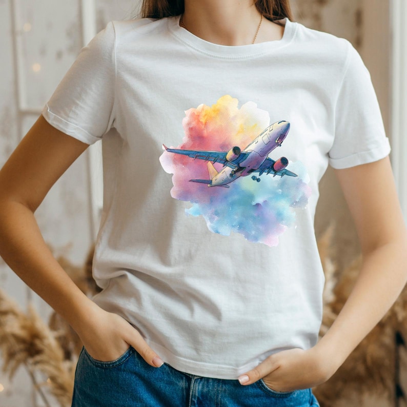 May include: White t-shirt featuring a colorful graphic of an airplane soaring through a vibrant cloud of pink, yellow, and blue hues. The airplane has a detailed design with red and yellow accents. The shirt is made of a soft material.