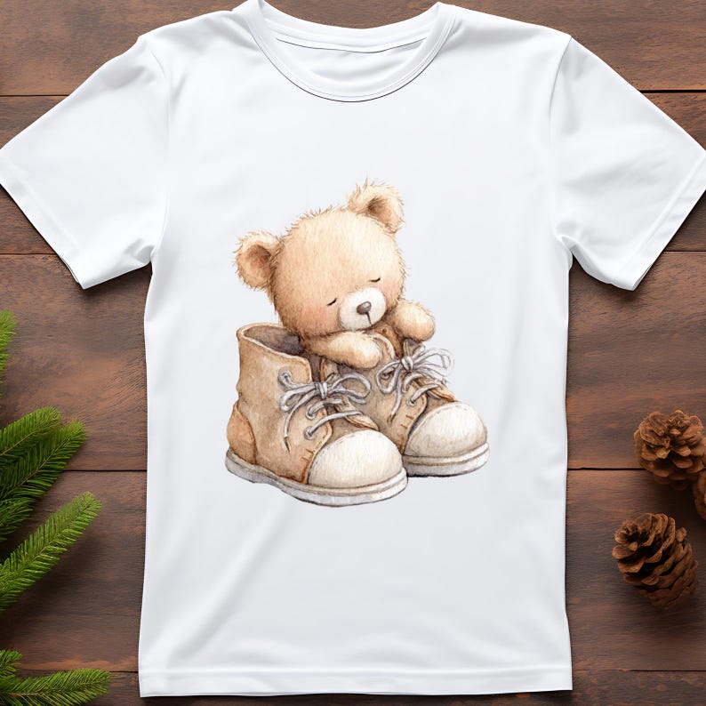 Puede incluir: Camiseta blanca con una ilustraci&oacute;n en acuarela de un oso de peluche dentro de un par de botas marrones. El oso es de color marr&oacute;n claro, con los ojos cerrados. Las botas tienen suelas y cordones blancos.