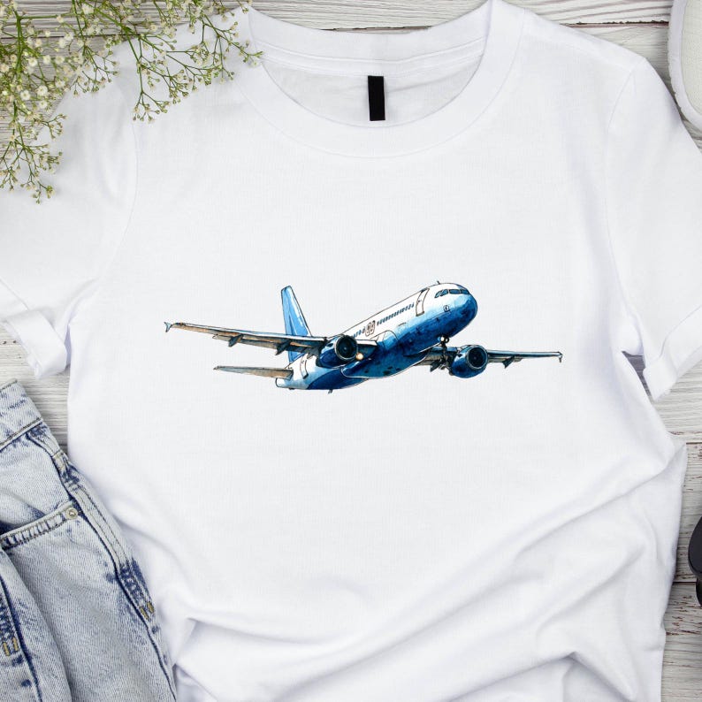 May include: White t-shirt featuring a watercolor illustration of a blue and white airplane in flight. The aircraft has detailed wings and engines, set against a clean white background. The design is centered on the shirt.