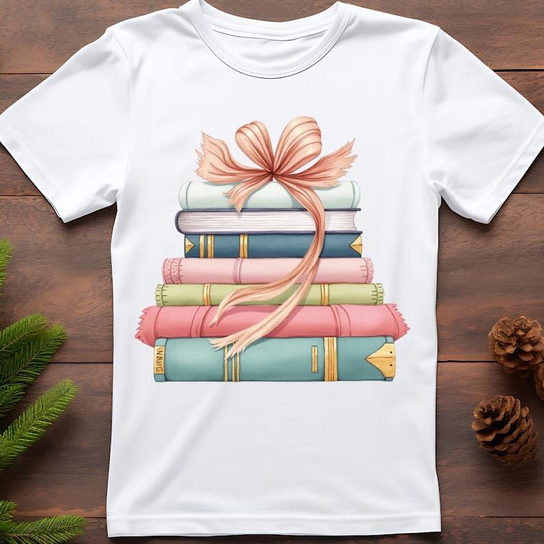 K&ouml;nnte beinhalten: Wei&szlig;es T-Shirt mit einem Aufdruck von einem Stapel bunter B&uuml;cher, die mit einer pfirsichfarbenen Schleife zusammengebunden sind. Die B&uuml;cher sind in Blau-, Rosa- und Gr&uuml;nt&ouml;nen gehalten und haben goldene Akzente. Ein verspieltes Design f&uuml;r B&uuml;cherliebhaber.