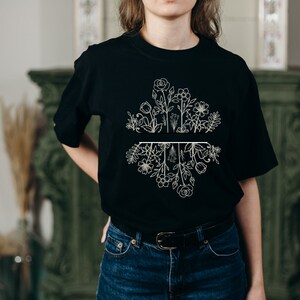 May include: A black t-shirt with a white floral design. The design features a variety of flowers and leaves, with a line dividing the top and bottom halves of the design.