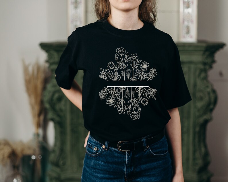 May include: A black t-shirt with a white floral design. The design features a variety of flowers and leaves, with a line dividing the top and bottom halves of the design.