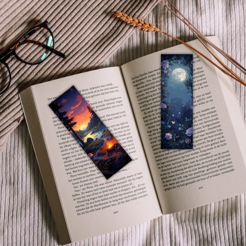May include: Two decorative bookmarks are placed on an open book. One shows a sunset over a river with trees, the other a moonlit forest with roses. The bookmarks are rectangular and colourful.