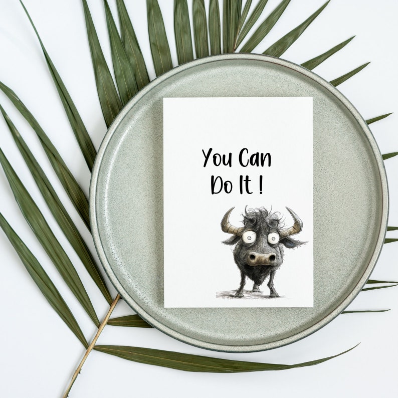 May include: A white card with the text "You Can Do It!" printed in black. A cartoon illustration of a black bull with large eyes is below the text.