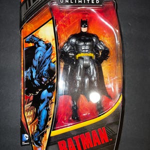 May include: A black and yellow Batman action figure in a plastic package. The figure is posed with its arms crossed and has a serious expression. The package has a red and orange background with the words "Batman Unlimited" printed on it.