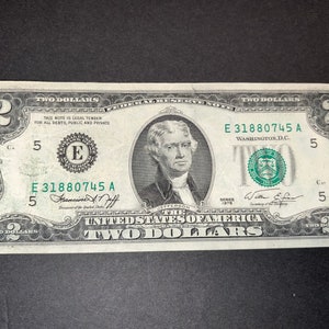 May include: A two dollar bill featuring a portrait of Thomas Jefferson, the text "United States of America", and the serial number "E 31880745 A".