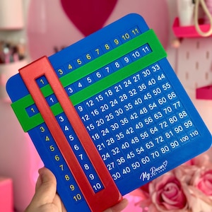May include: A blue multiplication chart board featuring a grid of numbers from 1 to 110, with a green horizontal slider and a red vertical slider. The board includes the text My Decor Spot Shop and is designed for educational math practice.